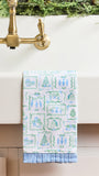 A white kitchen towel with a blue and green winter-themed pattern hangs from a brass faucet spout over a white sink.
