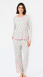 A woman modeling a two-piece long-sleeve pajama set with a white background and an all-over green pine tree pattern, accented with pink piping on the collar, cuffs, and waist, and pink side stripes on the pants.