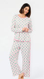 A woman modeling a two-piece long-sleeve pajama set with a pink and green pine tree pattern, standing against a plain white studio background.