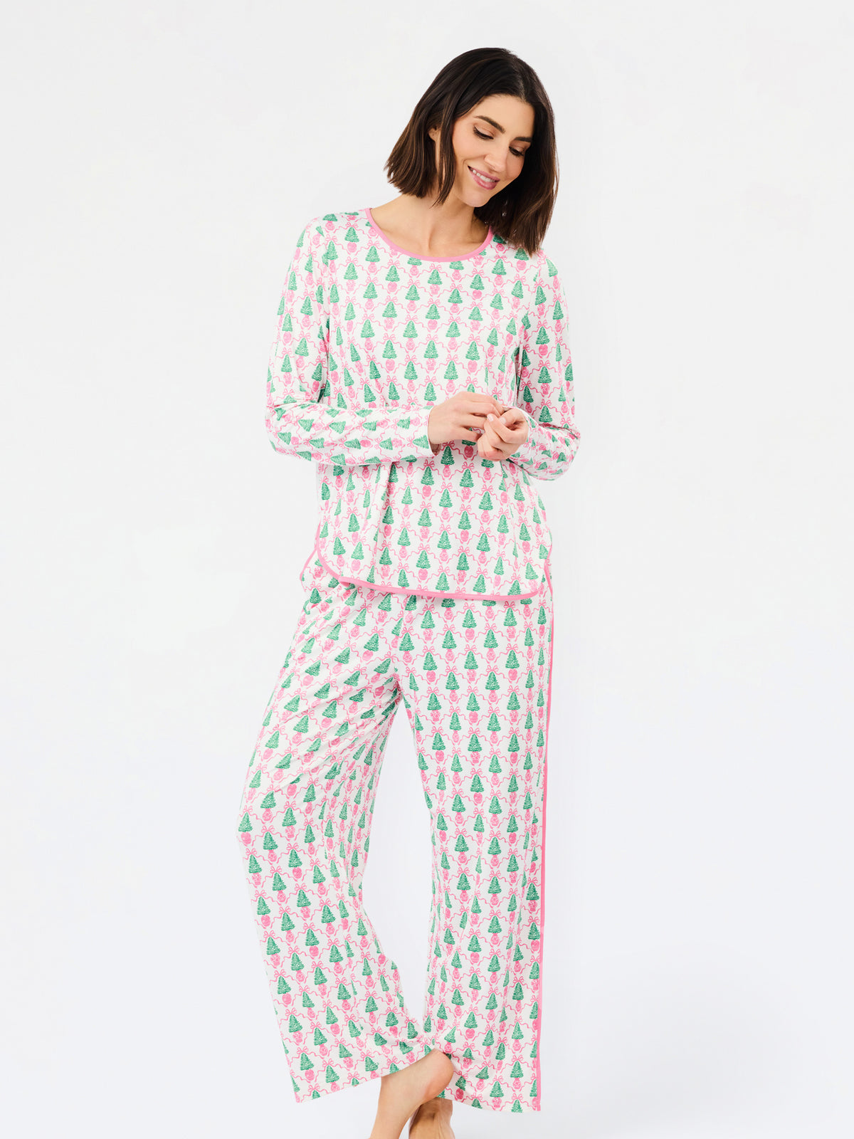 A woman modeling a two-piece long-sleeve pajama set with a pink and green pine tree pattern, standing against a plain white studio background.