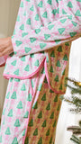 A person wearing a pink and gold holiday-themed pajama set with a green Christmas tree pattern, standing next to a decorated Christmas tree.
