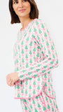 A woman wearing a matching long-sleeve pajama set with a pink and green Christmas tree pattern, photographed against a clean white background.
