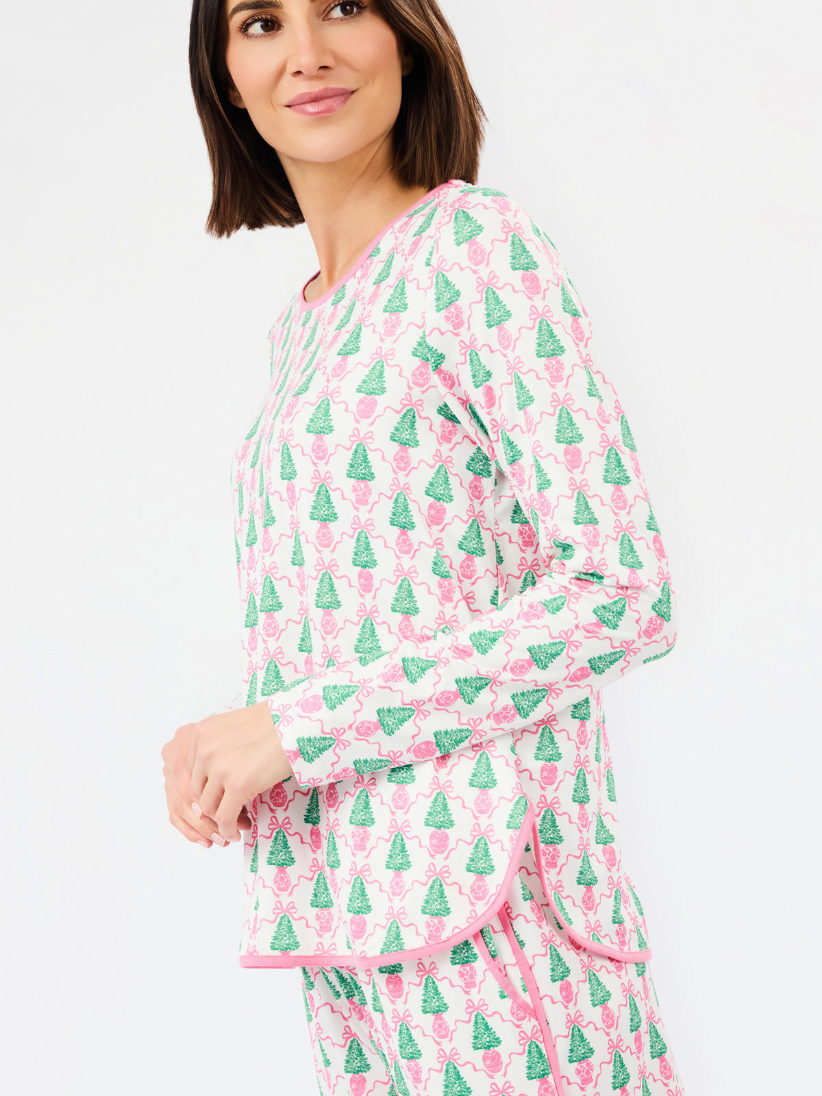 A woman wearing a matching long-sleeve pajama set with a pink and green Christmas tree pattern, photographed against a clean white background.