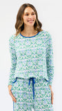 A woman modeling a matching long-sleeve top and pants pajama set with a green and blue floral pattern on a white background.