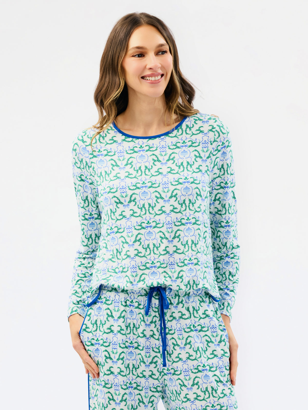 A woman modeling a matching long-sleeve top and pants pajama set with a green and blue floral pattern on a white background.