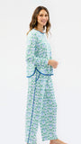 A woman modeling a matching two-piece holiday pajama set with a green and blue floral pattern and blue trim, standing against a plain white studio background.