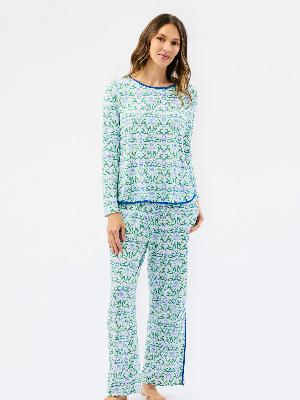 A woman modeling a matching two-piece pajama set with a light blue and green floral pattern and solid blue trim, photographed against a plain white studio background.