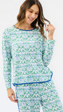 A woman modeling a matching long-sleeve pajama top and pants set with a green and blue floral pattern and blue trim, against a plain white studio background.