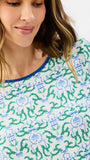 A close-up of a woman wearing a white long-sleeve top with a green and blue botanical pattern and a blue crew neckline.