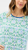 A woman wearing a white long-sleeve top with an all-over green and blue floral block print pattern and a contrasting blue crew neck trim.