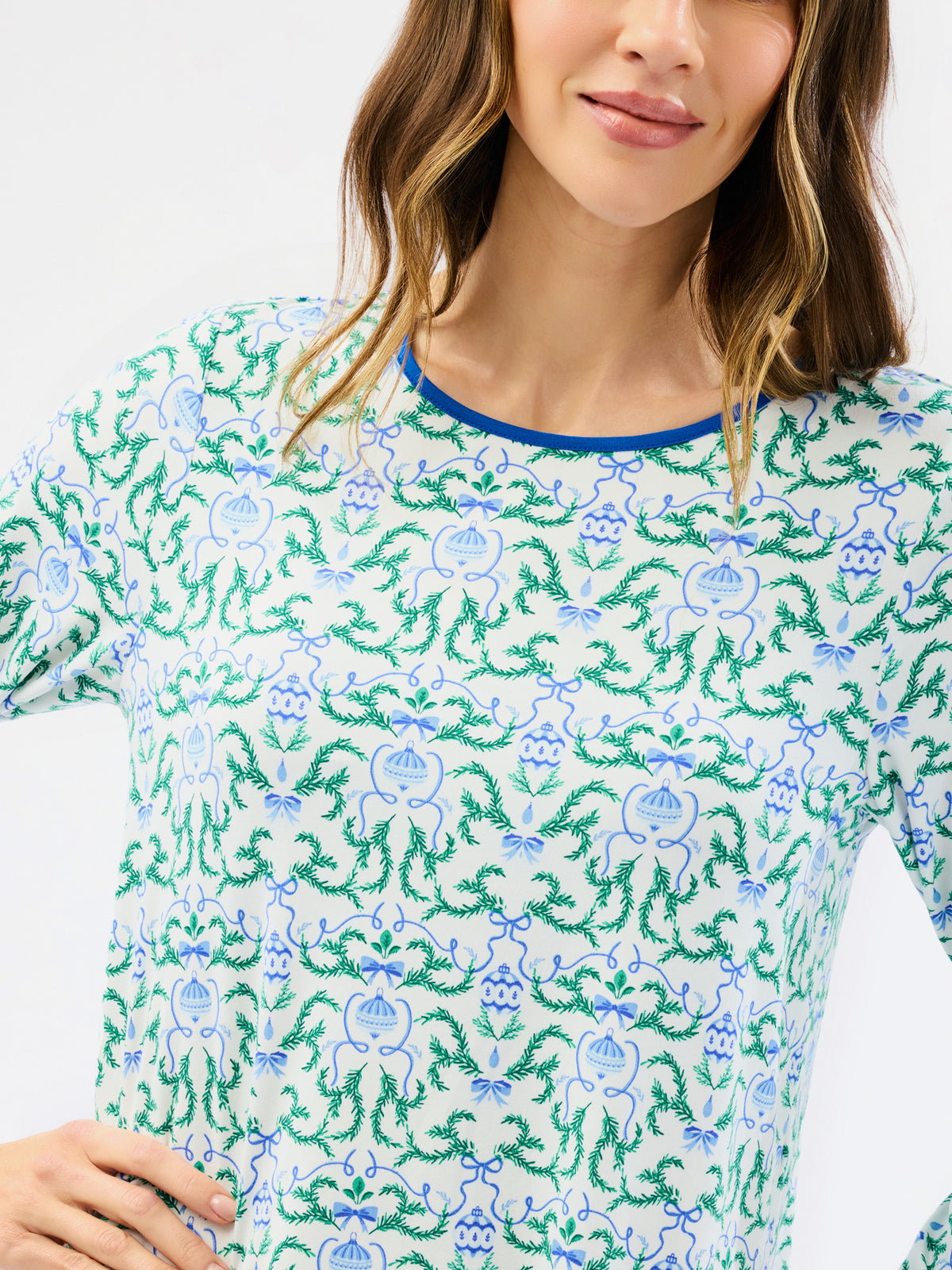 A woman wearing a white long-sleeve top with an all-over green and blue floral block print pattern and a contrasting blue crew neck trim.