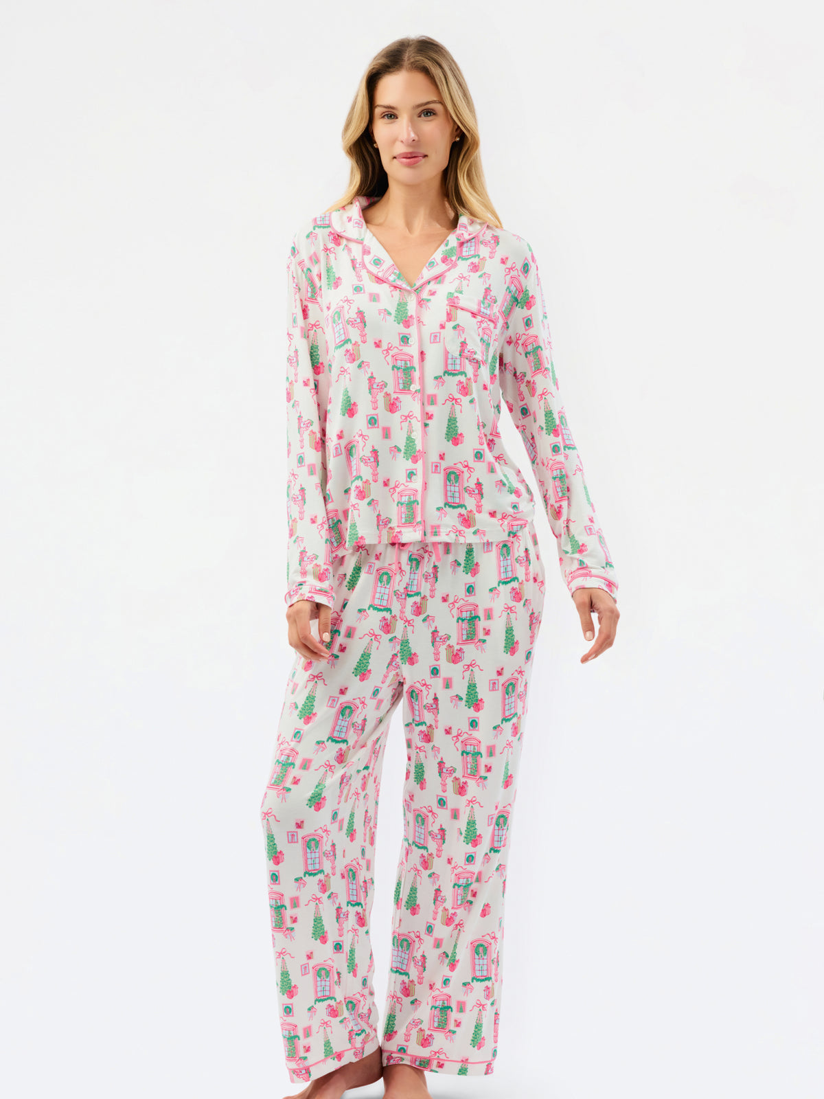 A woman modeling a matching long-sleeve button-front pajama top and wide-leg pajama pants set with a pink and green illustrated print on a white base, photographed against a plain white studio background.