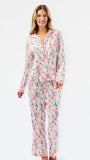 A woman modeling a matching long-sleeve pajama set with a pink and green illustrated print on a white background, photographed against a clean white studio backdrop.