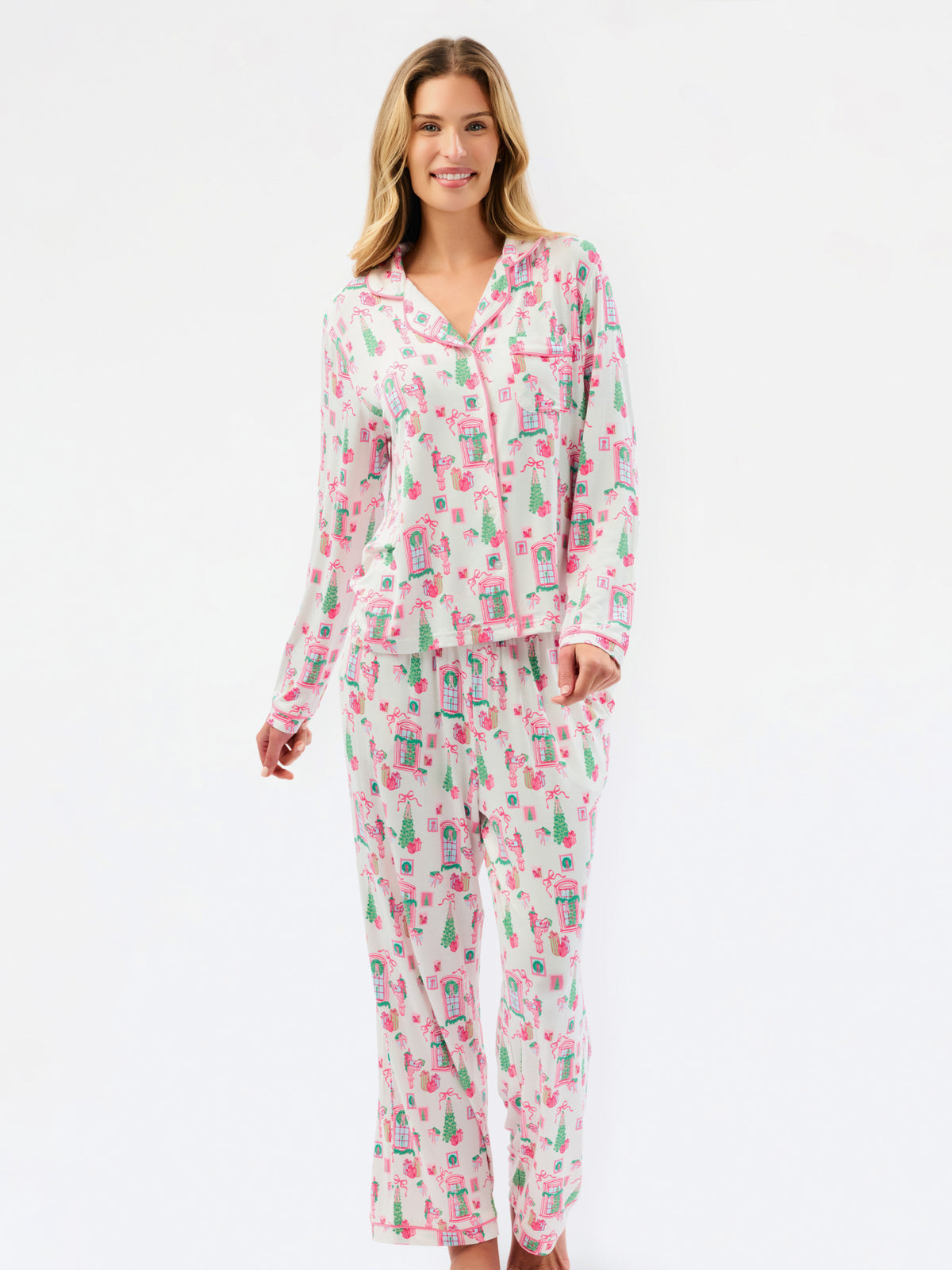 A woman modeling a matching long-sleeve pajama set with a pink and green illustrated print on a white background, photographed against a clean white studio backdrop.