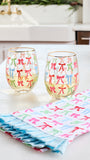 Two clear stemless wine glasses with gold rims decorated with colorful bow patterns, set on a white countertop next to a matching folded cloth napkin with ruffled edges.