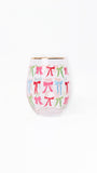 A clear stemless wine glass with a gold rim, decorated with a repeating pattern of colorful bows in pink, green, and blue on a white background.