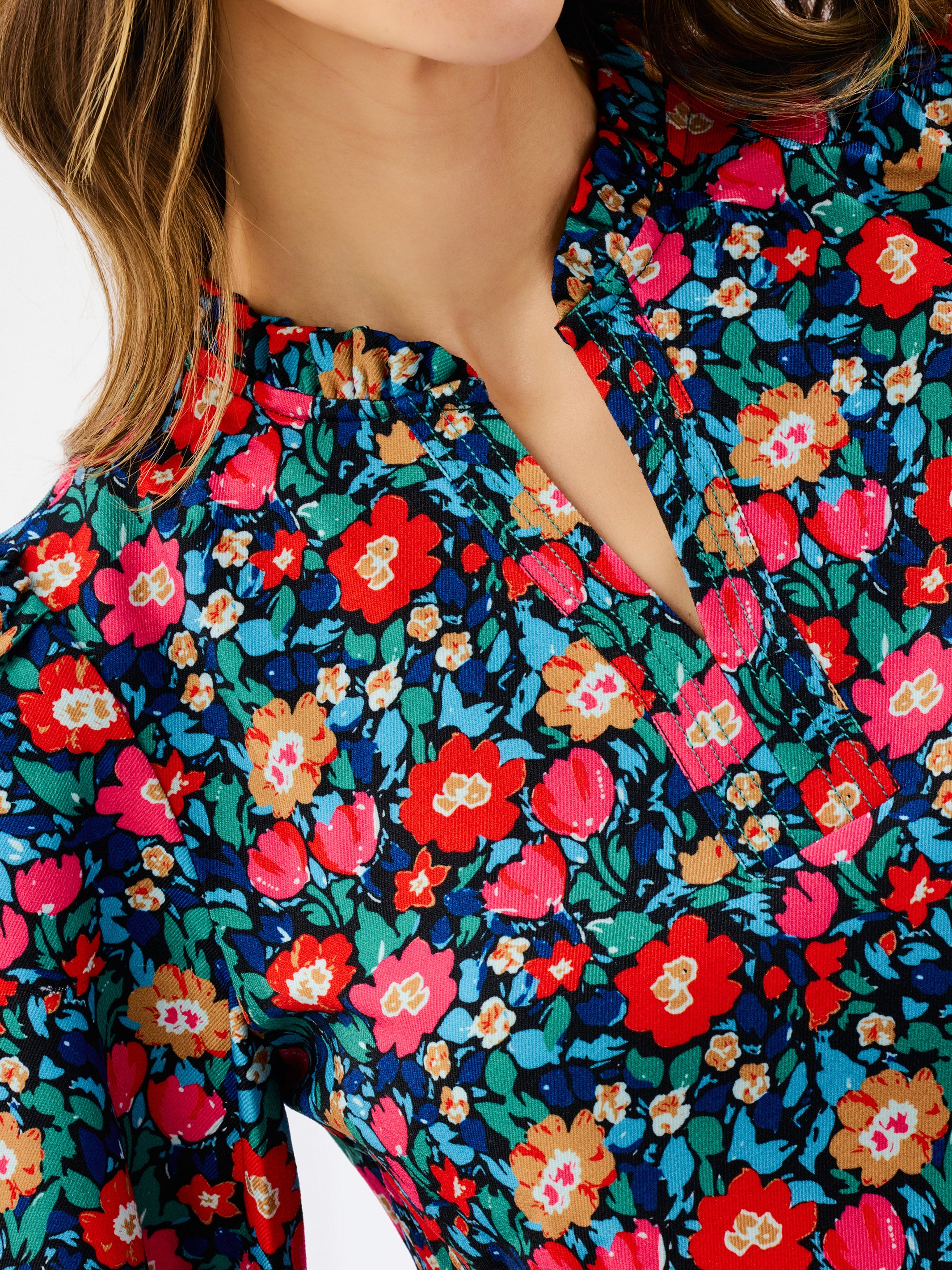 A woman modeling a long-sleeve floral blouse with a split neckline, paired with dark blue jeans, against a plain white studio background.