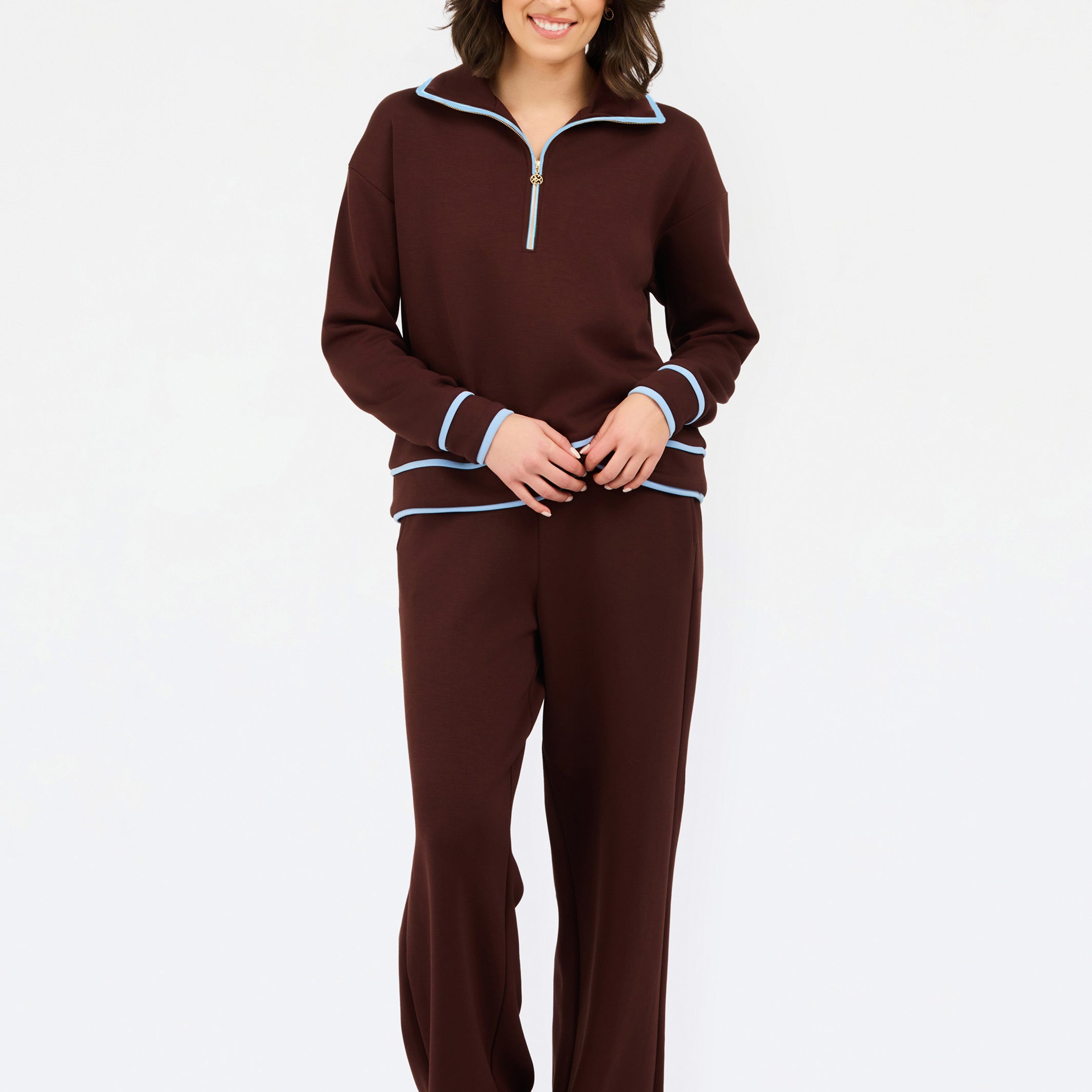 A woman modeling a matching two-piece lounge set in deep burgundy, featuring a quarter-zip long-sleeve top with light blue and white striped trim, and matching wide-leg pants.