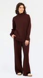 A woman wearing an oversized dark brown mock neck sweatshirt and matching sweatpants, photographed against a clean white studio background.