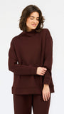 A woman wearing an oversized dark brown mock neck sweatshirt and matching sweatpants, photographed against a clean white studio background.