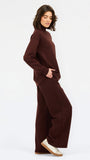 A woman wearing an oversized dark brown mock neck sweatshirt and matching sweatpants, photographed against a clean white studio background.