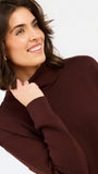 A woman wearing an oversized dark brown mock neck sweatshirt and matching sweatpants, photographed against a clean white studio background.