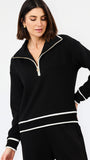 A woman wearing a black long-sleeve quarter-zip sweatshirt with white contrast trim and matching black pants, photographed against a clean white studio background.