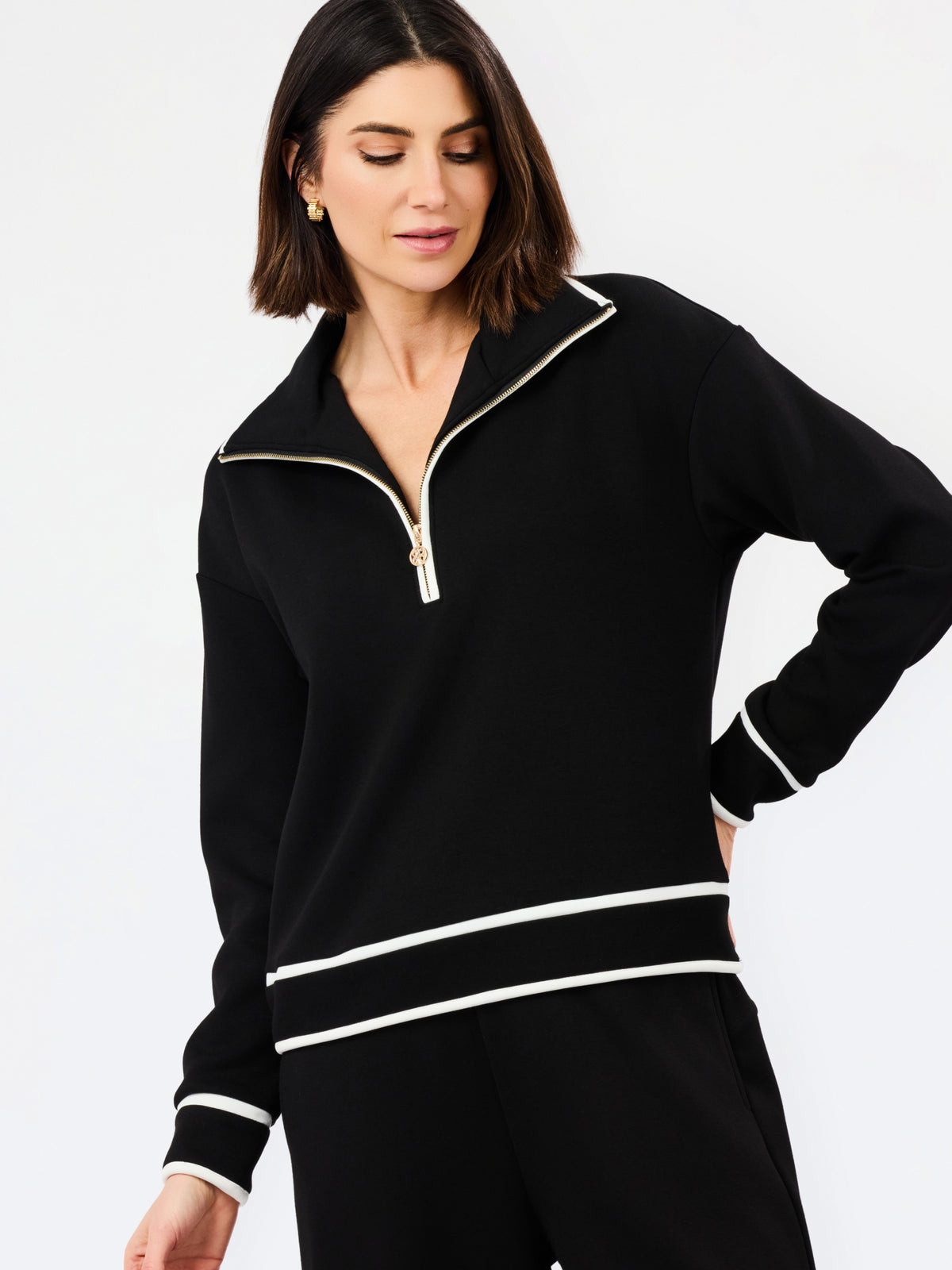 A woman wearing a black long-sleeve quarter-zip sweatshirt with white contrast trim and matching black pants, photographed against a clean white studio background.