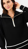 A woman wearing a black long-sleeve quarter-zip pullover with white contrast piping details on the collar, zipper track, cuffs, and hem, set against a plain white studio background.