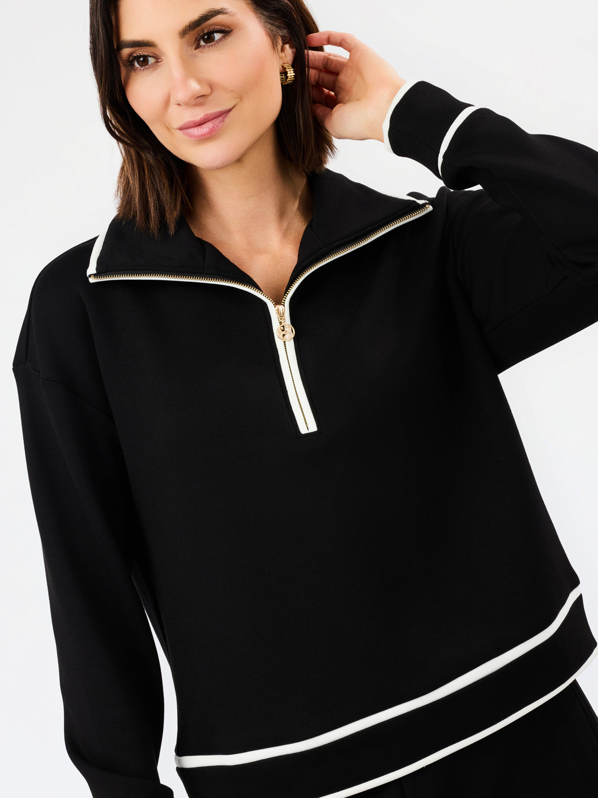 A woman wearing a black long-sleeve quarter-zip pullover with white contrast piping details on the collar, zipper track, cuffs, and hem, set against a plain white studio background.