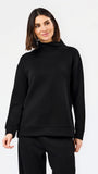 A woman modeling a black long-sleeve mock neck sweatshirt and matching black pants against a plain white studio background.