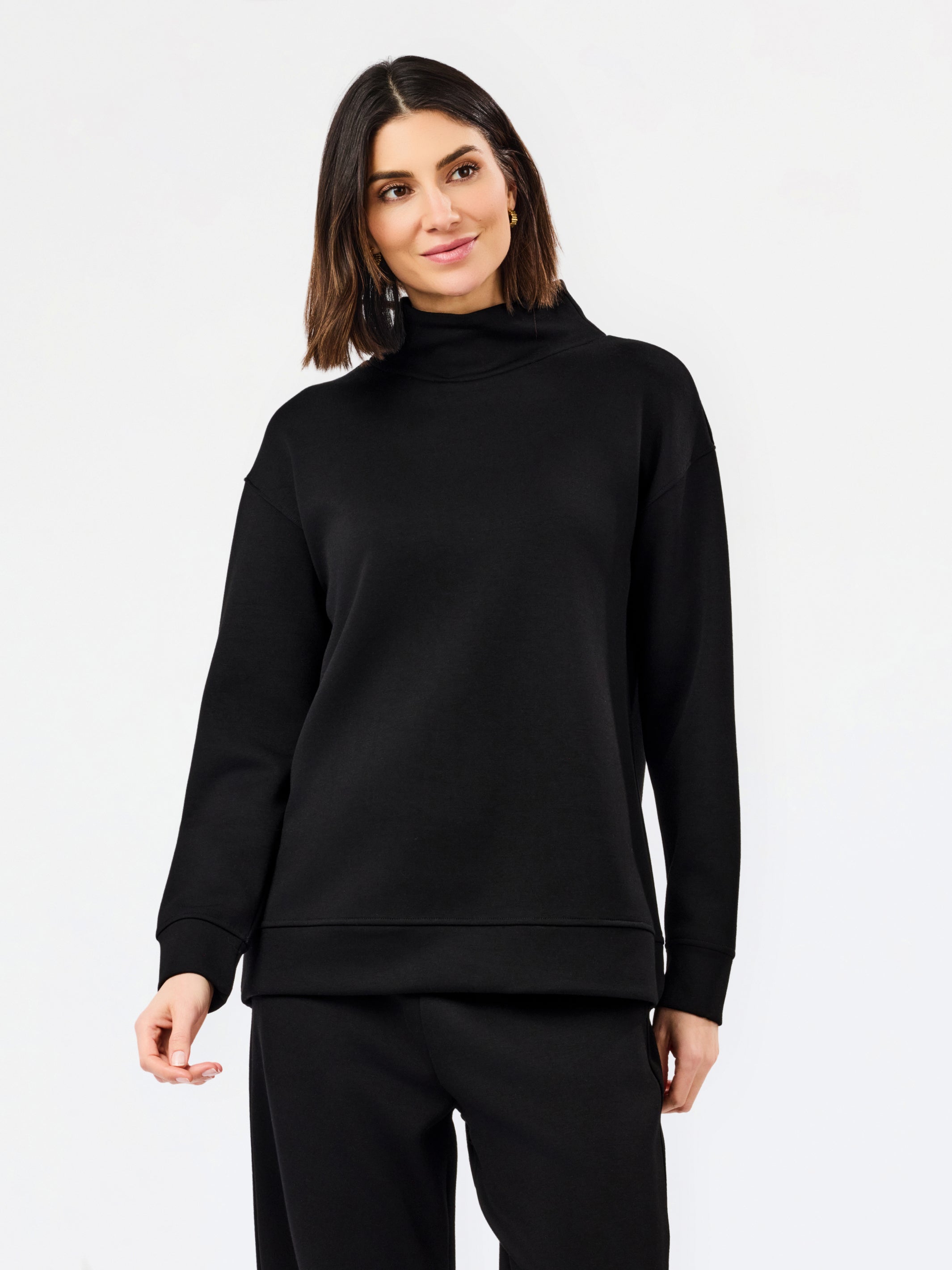 A woman modeling a black long-sleeve mock neck sweatshirt and matching black pants against a plain white studio background.