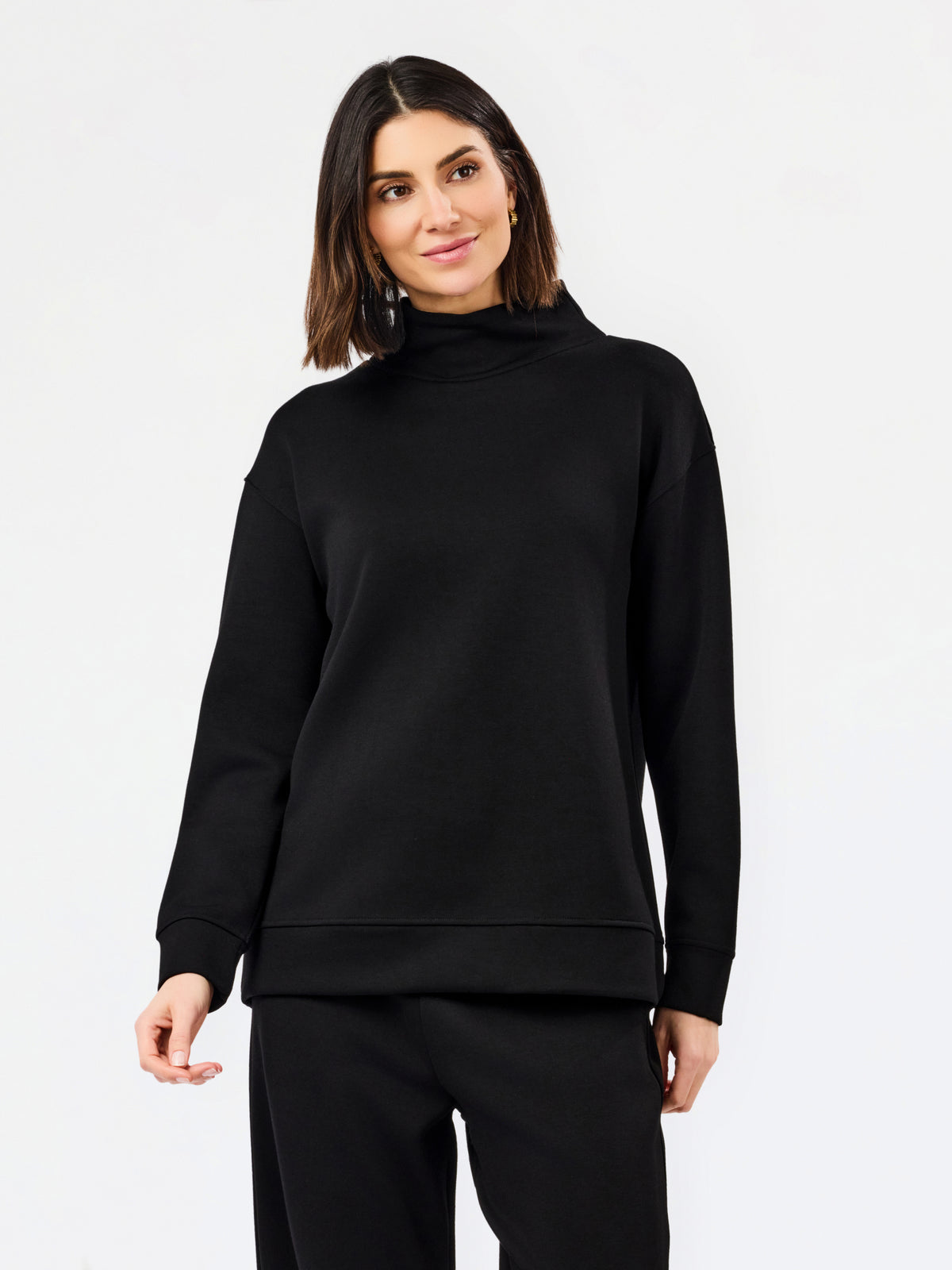 A woman modeling a black long-sleeve mock neck sweatshirt and matching black pants against a plain white studio background.