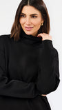 A woman wearing a black long-sleeve turtleneck top, posing against a clean white studio background.