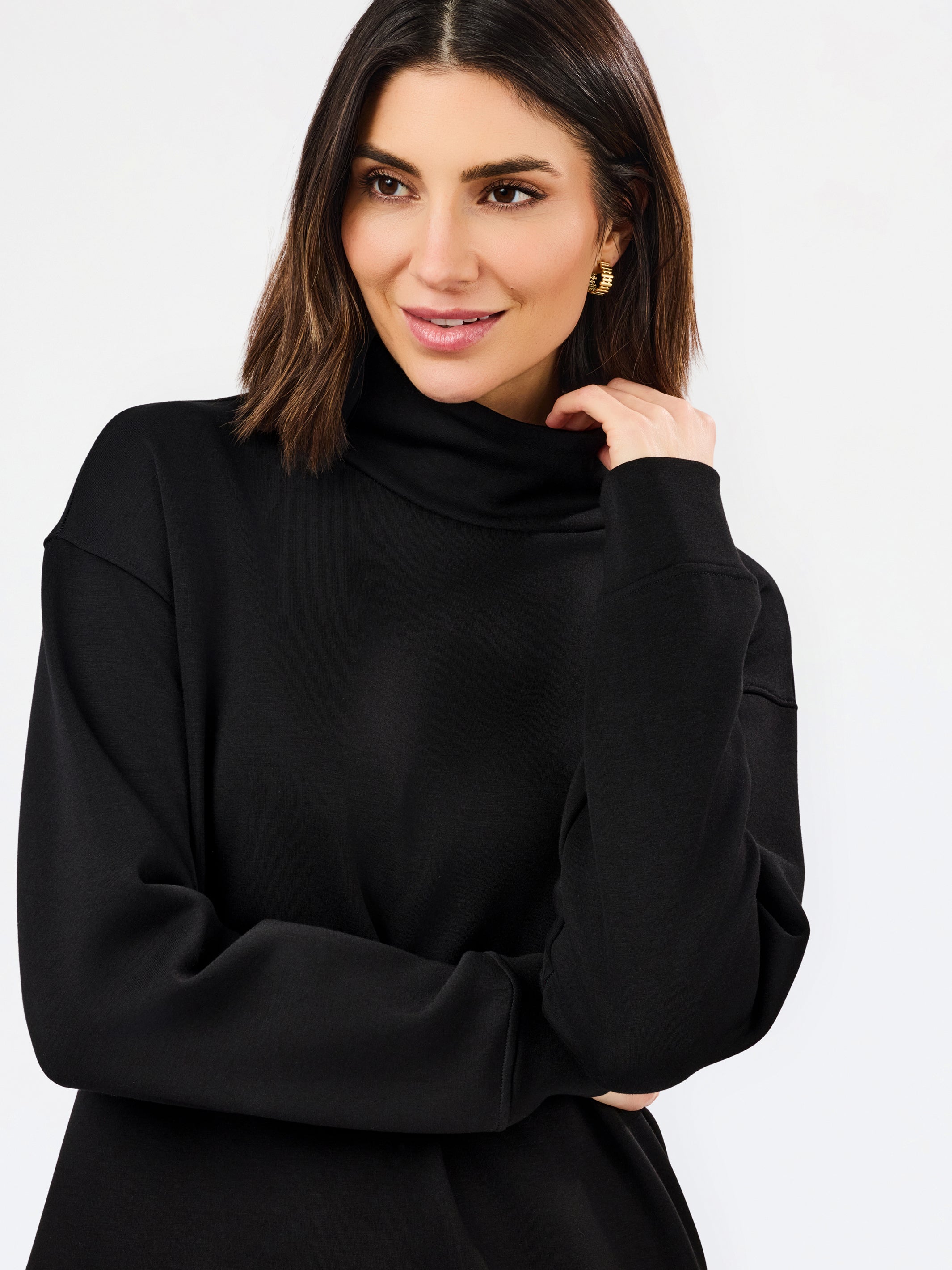 A woman wearing a black long-sleeve turtleneck top, posing against a clean white studio background.