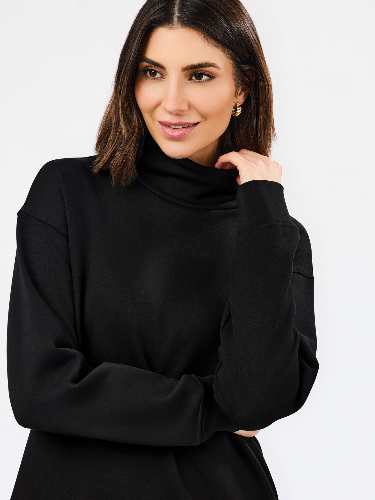 A woman wearing a black long-sleeve turtleneck top, posing against a clean white studio background.