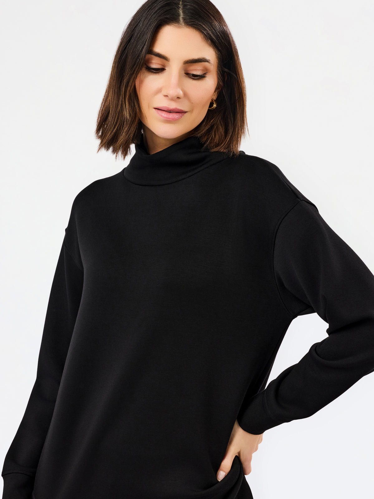 A woman wearing an oversized black long-sleeve turtleneck top, photographed against a clean light gray studio background.