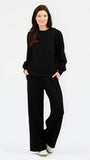 A woman modeling a black long-sleeve crewneck sweatshirt and matching black wide-leg pants against a plain white studio background.