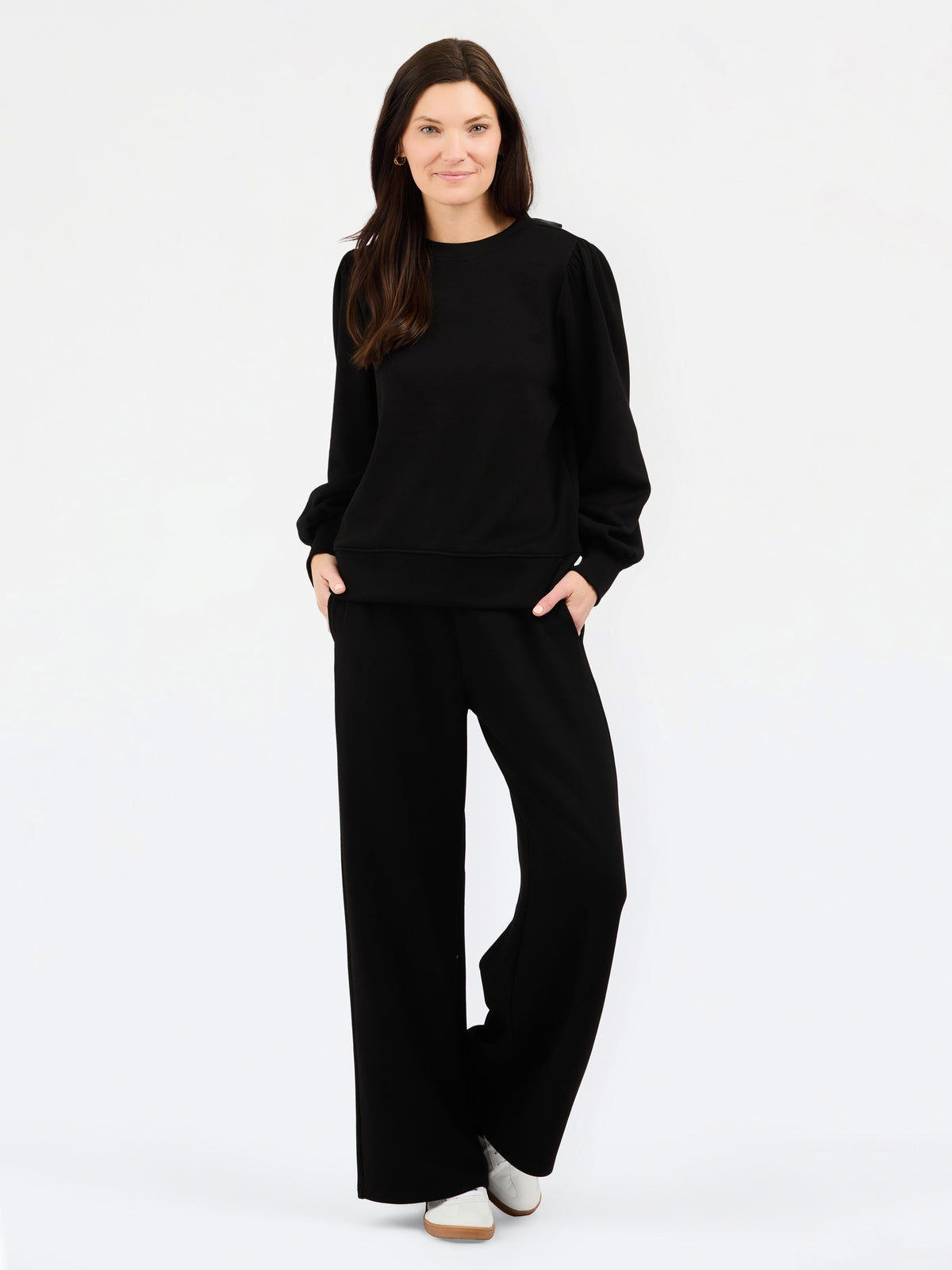 A woman modeling a black long-sleeve crewneck sweatshirt and matching black wide-leg pants against a plain white studio background.