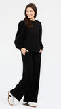 A woman modeling a black long-sleeve sweatshirt with balloon sleeves and matching black wide-leg pants, paired with white sneakers, against a plain white studio background.