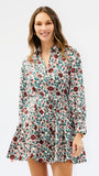 A woman modeling a long-sleeve floral mini dress with a button-up front and ruffled hem, set against a plain light gray studio background.