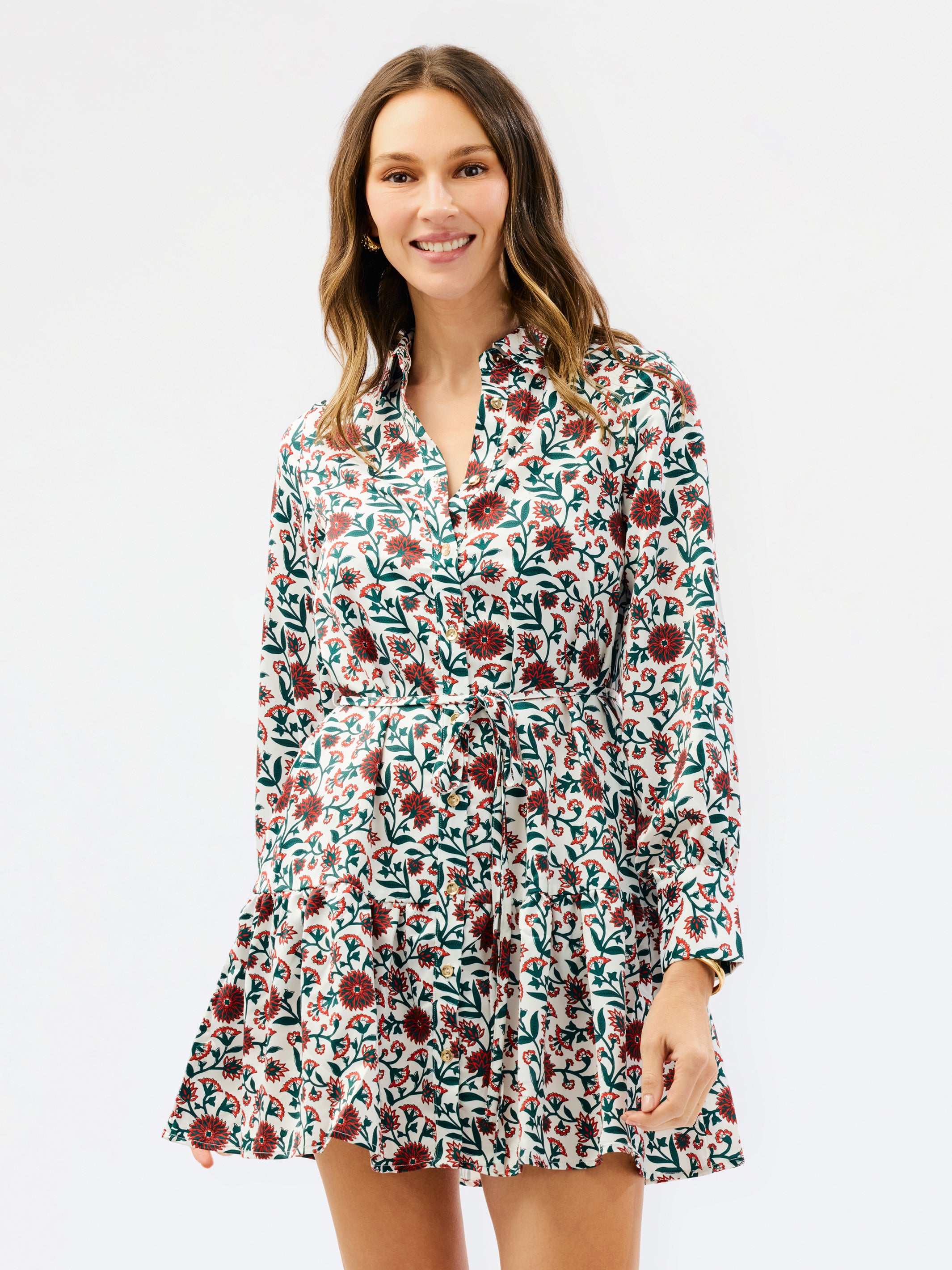 A woman modeling a long-sleeve floral mini dress with a button-up front and ruffled hem, set against a plain light gray studio background.