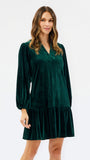 Woman wearing a festive green velvet long sleeve short dress with a tiered skirt on a white background