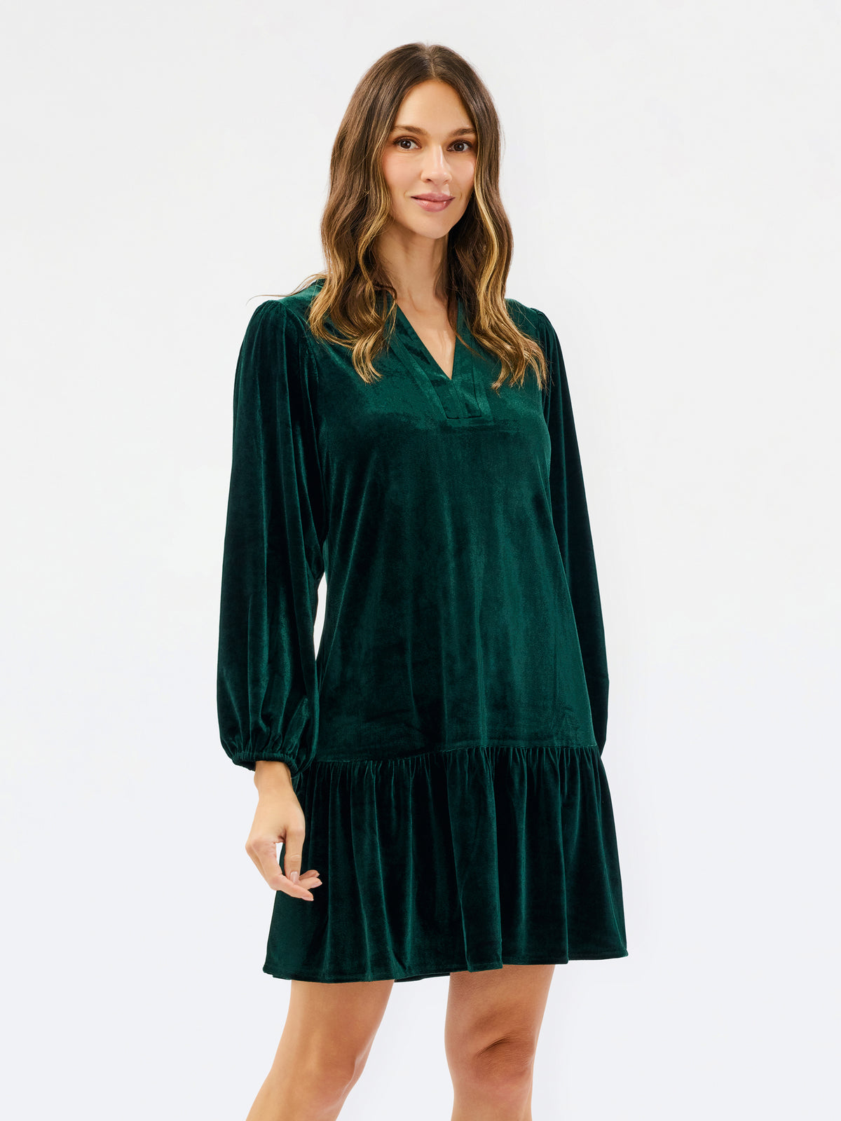 Woman wearing a festive green velvet long sleeve short dress with a tiered skirt on a white background