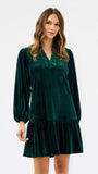 Woman wearing a festive green velvet long sleeve short dress with a tiered skirt on a white background
