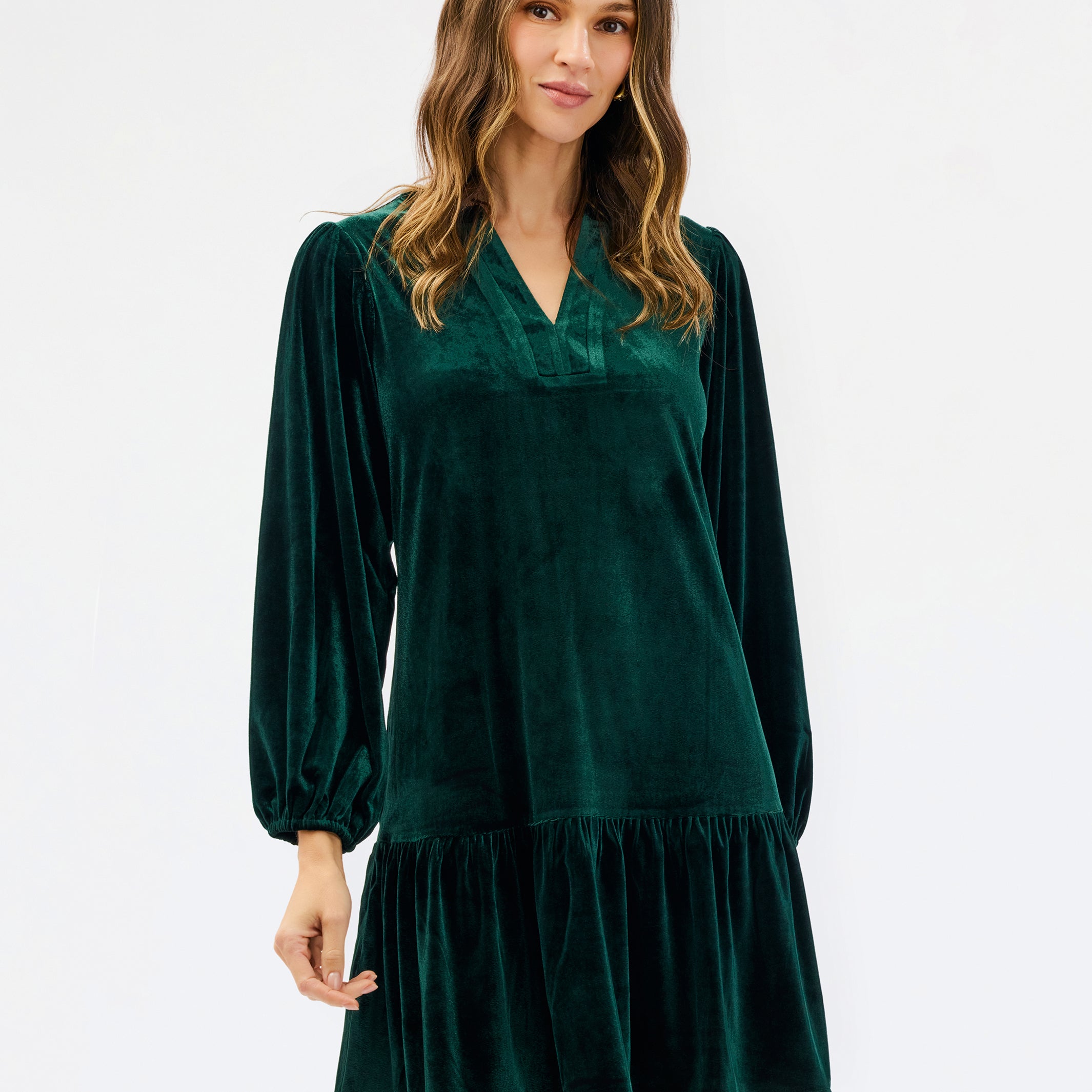 Woman wearing a festive green velvet long sleeve short dress with a tiered skirt on a white background