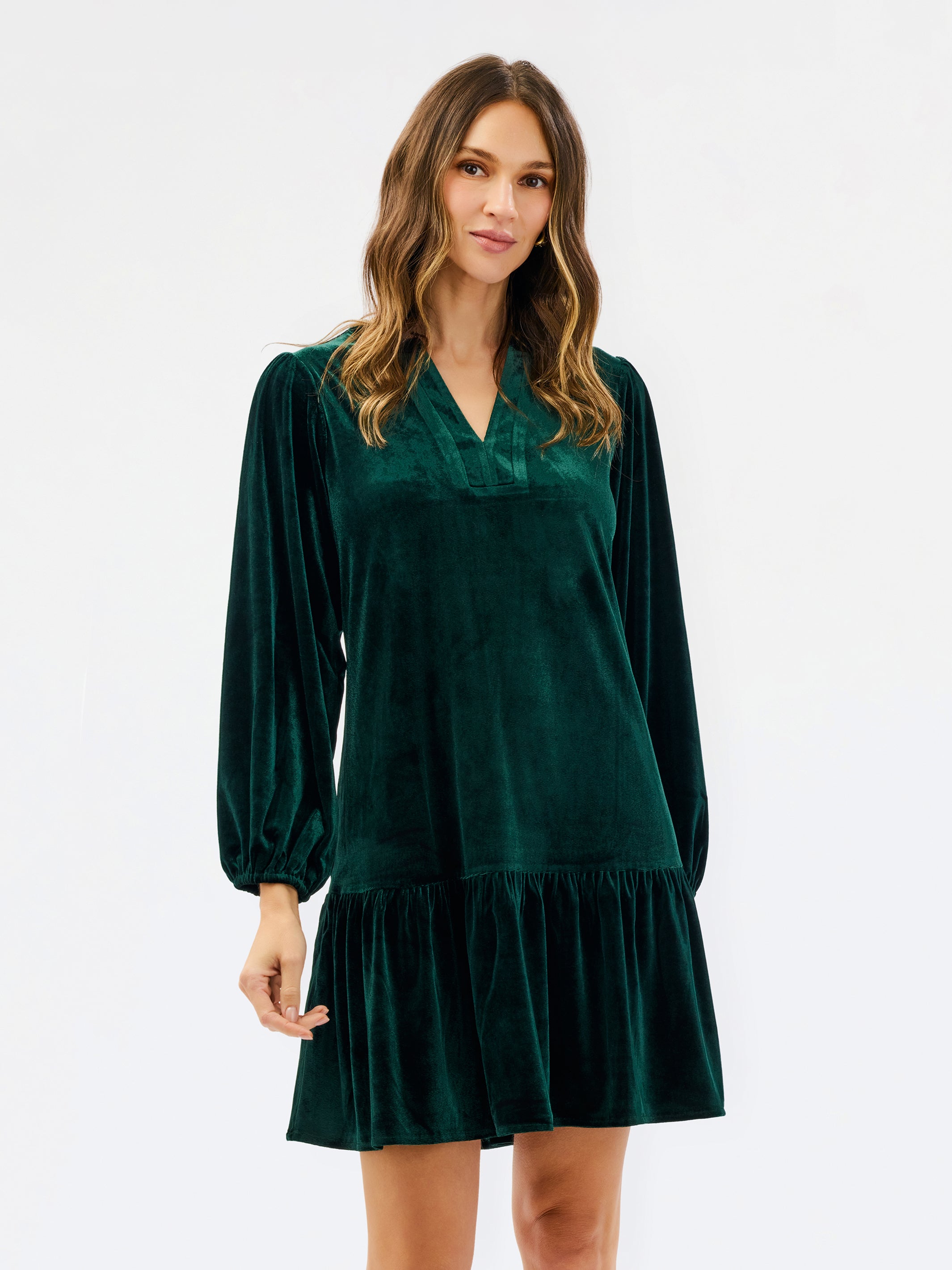 Woman wearing a festive green velvet long sleeve short dress with a tiered skirt on a white background