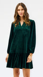 Woman wearing a festive green velvet long sleeve short dress with a tiered skirt on a white background