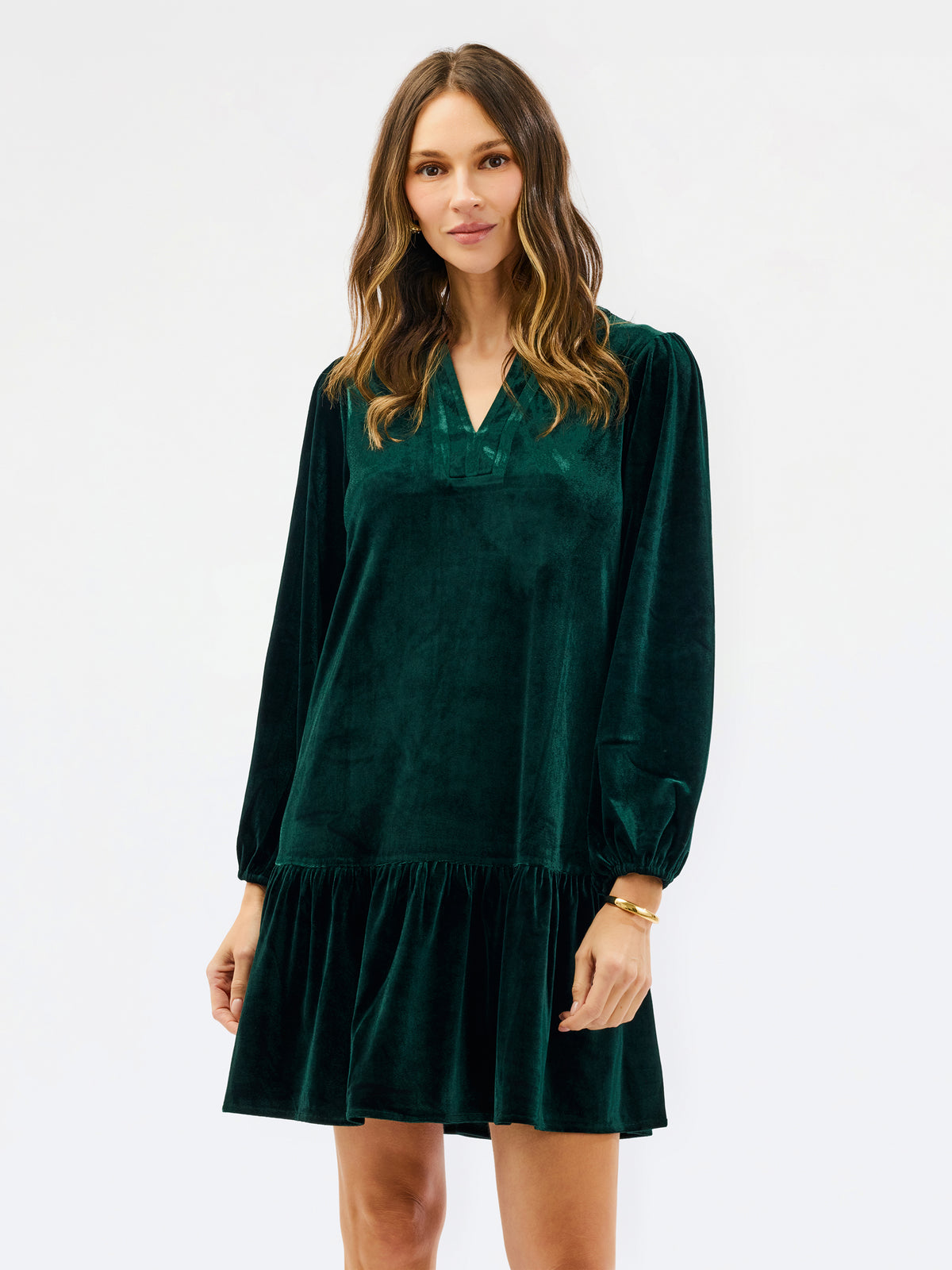 Woman wearing a festive green velvet long sleeve short dress with a tiered skirt on a white background