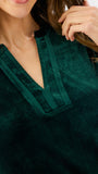 Woman wearing a festive green velvet long sleeve short dress with a tiered skirt on a white background